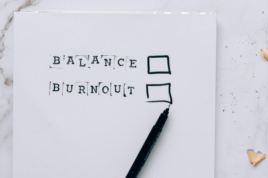 A sheet of paper that lists "Balance" and "Burnout" in stamped letters, next to hand-drawn check boxes next to them, indicating that the viewer can choose one of them. There is a black pen underneath the check boxes. The paper is on a marble countertop with pencil shavings to the right.