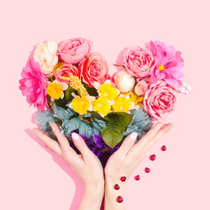 Hands holding an arrangement of colorful flowers in a heart shape to inspire you to ask for love